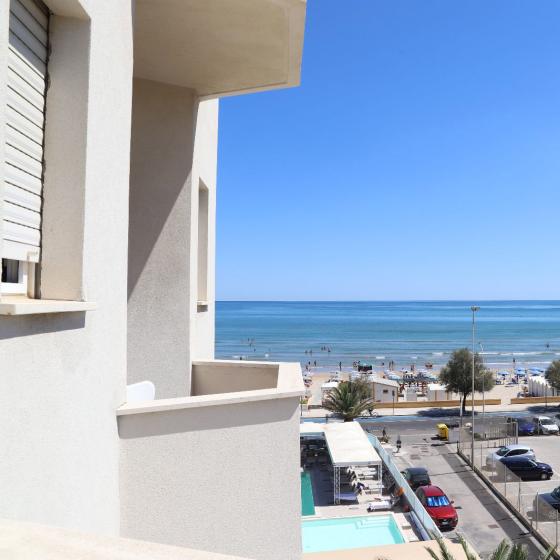 Vista mare con spiaggia, parcheggio e piscina da un edificio bianco.