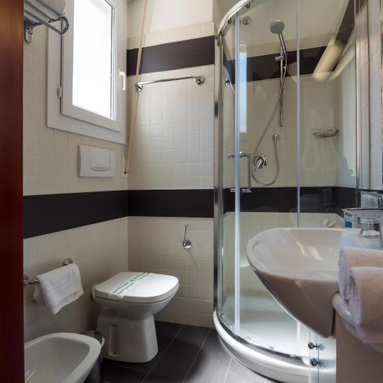Bagno moderno con doccia, bidet e sanitari, piastrelle scure e finestra luminosa.