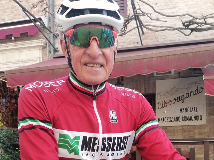 Ciclista sorridente, abbigliamento rosso, atmosfera accogliente di un borgo italiano.